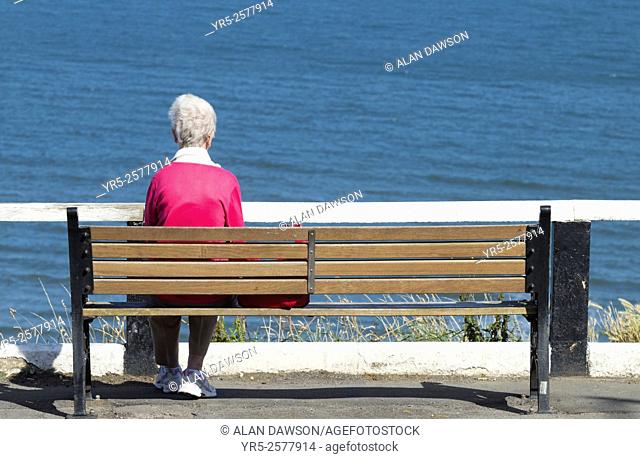 Elderly woman sitting on seat overlooking sea at Saltburn by the Sea, North Yorkshire, England, United Kingdom