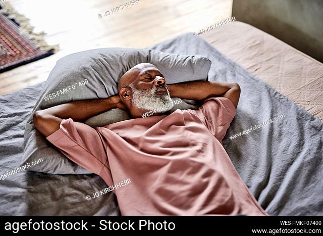 Bald man with eyes closed resting on bed at home