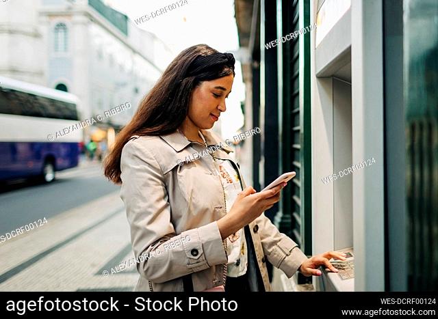 Woman using atm machine and mobile phone