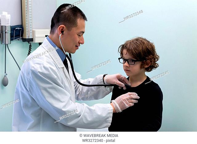 Young asian male doctor examining caucasian boy patient with stethoscope in clinic