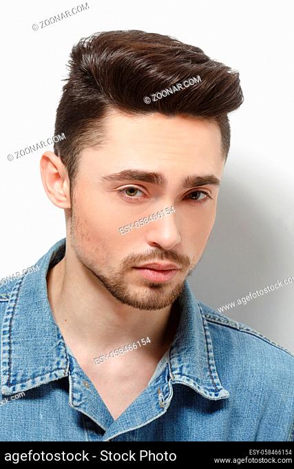 Portrait of young model man demonstrating his gorgeous and luxurious hair in studio. Handsome male in jeans shirt over shite background