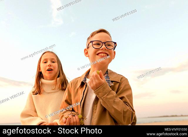 Happy boy with sister standing under sky at beach
