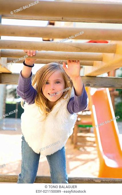 kid girl playing in playground hanging from wood bars