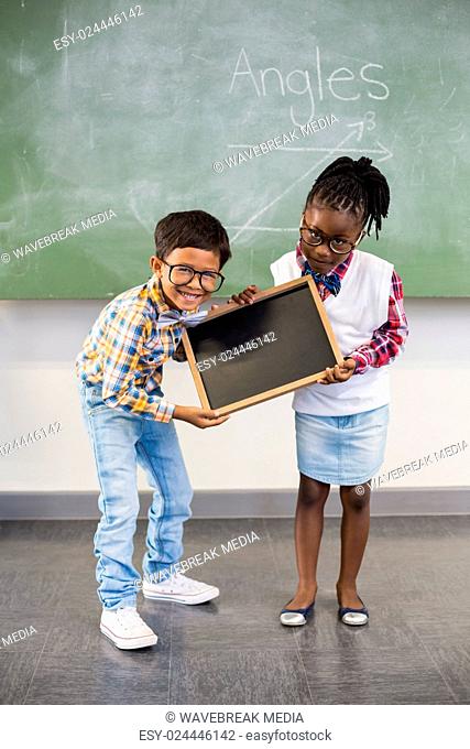Portrait of two smiling school kids holding slate in classroom