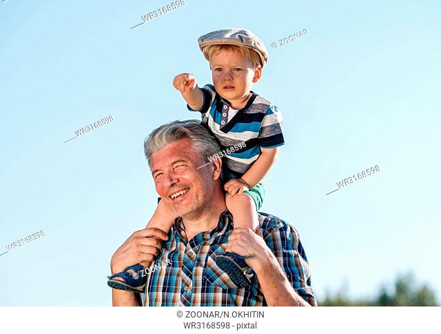 Grandfather carries grandson toddler boy on his shoulders