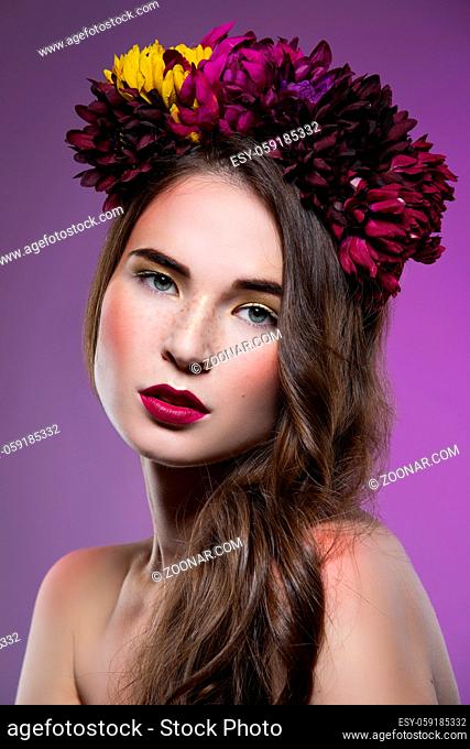 Beautiful young brunette woman with floral head piece in hair over purple background. Beauty shot
