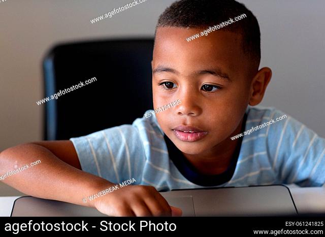 Close-up of african american elementary schoolboy using laptop while sitting at desk in school