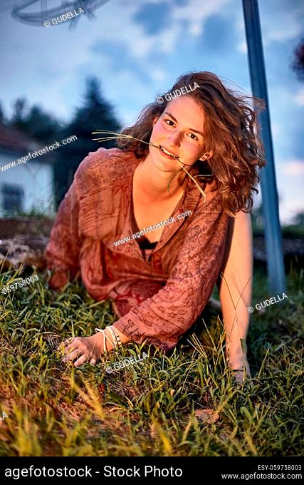 Young woman posing in the grass with grass blade between teeth