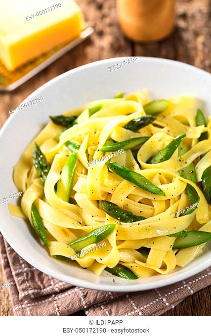 Fresh homemade pasta dish of fettuccine or tagliatelle, green asparagus, garlic and lemon juice in bowl, ground black pepper on top (Selective Focus