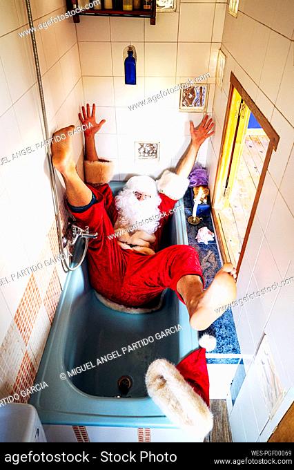 Man wearing Santa Claus costume falling in bathtub at home