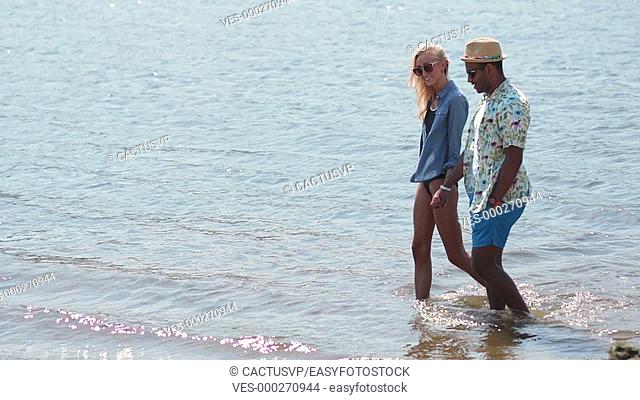 Couple holding hands walking in water on beach