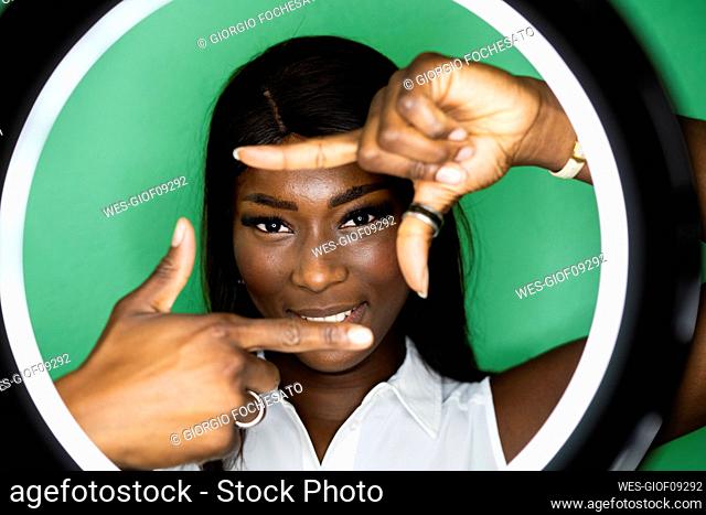 Smiling young woman making finger frame against green background