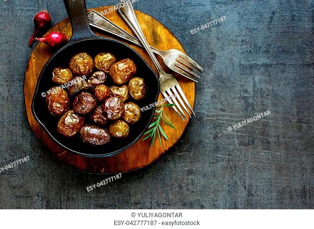 Fried Country-style baby potatoes in vintage cast iron pan on wooden board over black concrete background, copy space. Healthy food concept