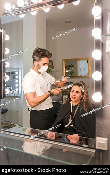 Mirror reflection of male expert dyeing female customer hair at salon