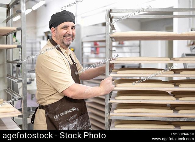 Confident baker posing with rack of fresh bread loaf at bakery. High quality photo
