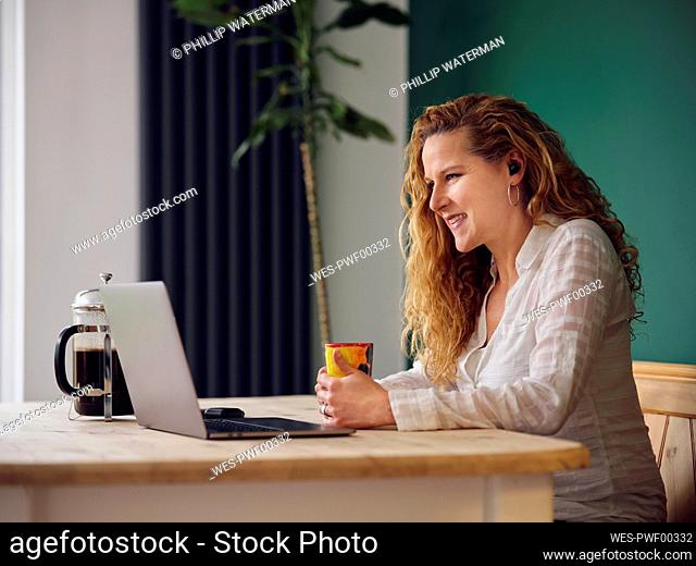Smiling woman having coffee while looking at laptop