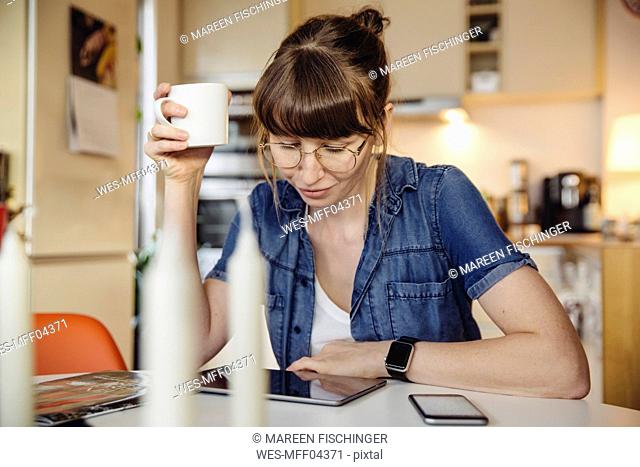 Woman sitting with cup of coffee at table in the kitchen using tablet