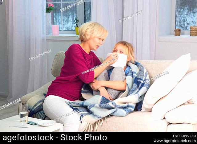 Mother taking care of her sick child, wiping her face with handkerchief. Caring mom staying with ill daughter