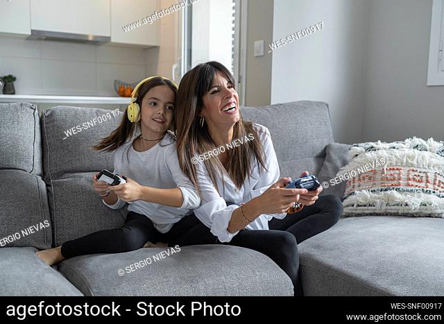 Smiling mother and daughter playing video games together at home