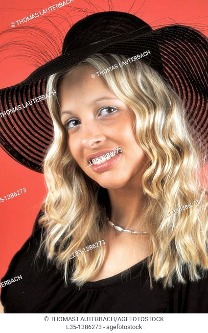 Young blonde woman in a black hat against a red background