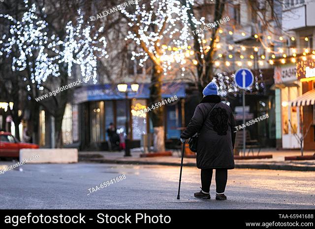 RUSSIA, LUGANSK - 20 de diciembre de 2023: Una mujer pasa por los árboles adornados con luces de cuerda en la Plaza de los Héroes de Guerra
