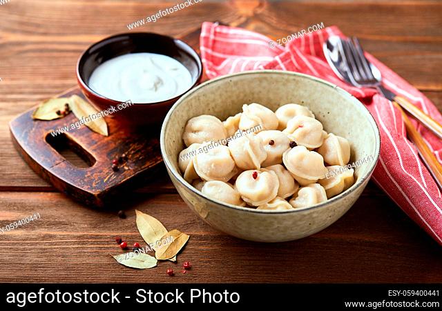 Dumplings stuffed with meat, pelmeni, ravioli, dumplings. Traditional homemade Russian pelmeni meat dumplings with sour cream over wooden background