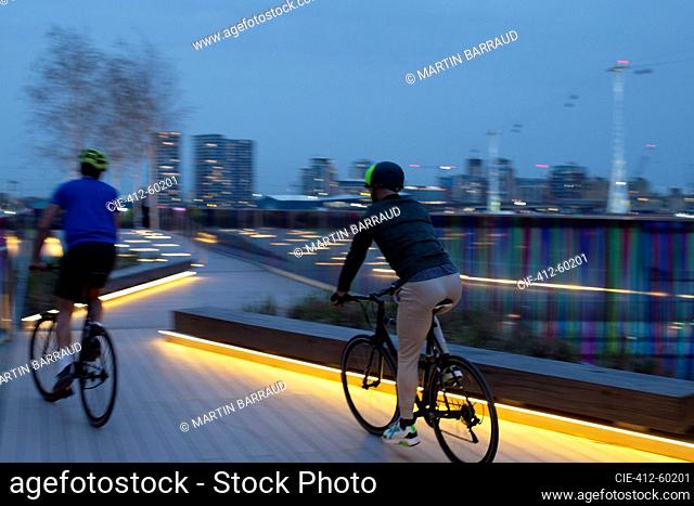 Men riding bicycles on illuminated boardwalk in city at night, London