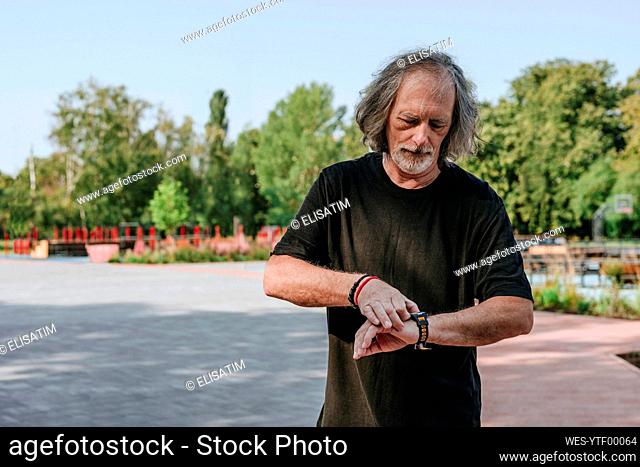 Senior man checking pulse rate on smart watch in park