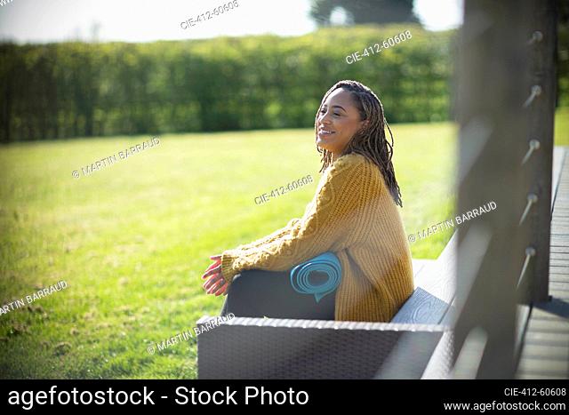 Happy young woman with yoga mat on sunny bench