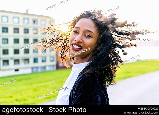 Portrait of young woman with ringlets tossing her hair at backlight