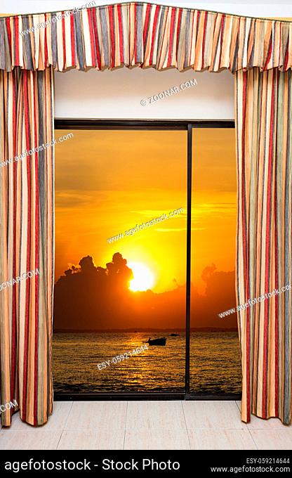 beautiful sunset on the sea view from the window with curtains open