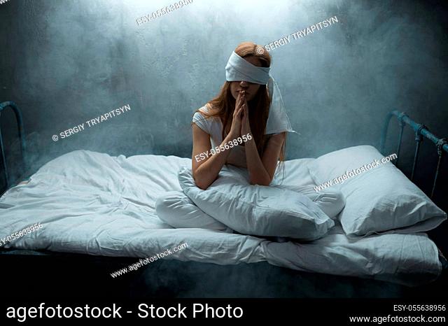 Blindfolded crazy woman sitting in bed, dark room on background. Psychedelic female person having problems every night, depression and stress, sadness