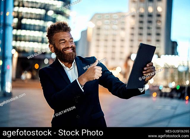 Smiling male freelancer gesturing thumbs up while taking selfie through digital tablet