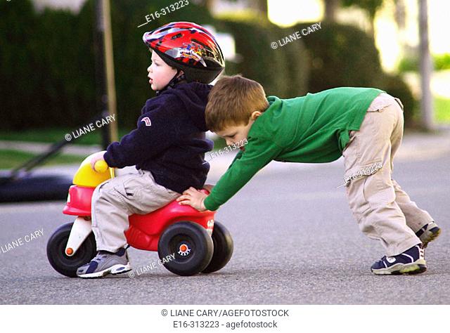pushing boy on toy tricycle