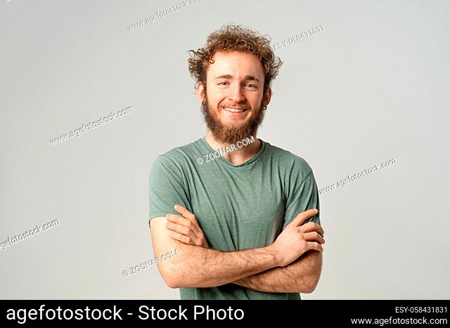 Handsome young man with curly hair in olive t-shirt looking at camera isolated on white background. Portrait of smiling young man with hands folded
