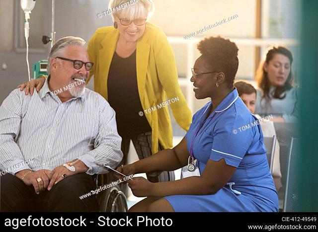 Female nurse talking with senior male patient in wheelchair in clinic lobby
