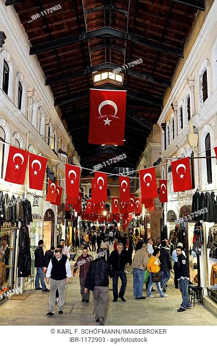 Roofed alley with shops, crowed with people, hanging Turkish flags, Kapali Carsi Grand Bazaar, Istanbul, Turkey