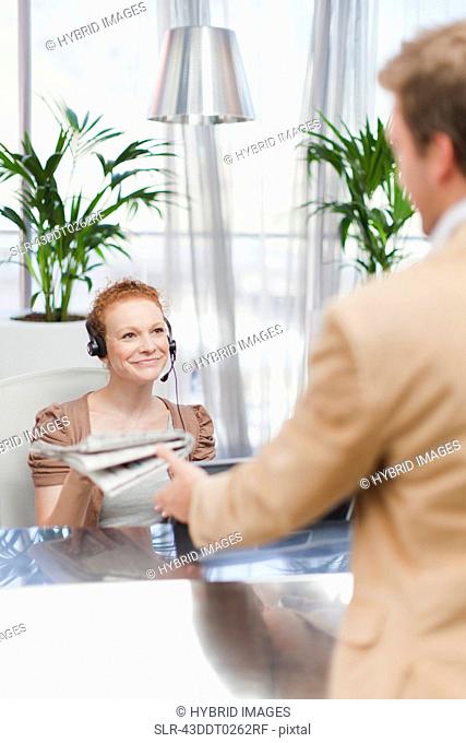 Receptionist giving newspaper to man