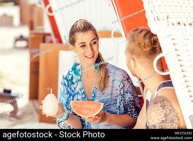 Young smiling woman holding coconut water and watermelon looking at her boyfriend
