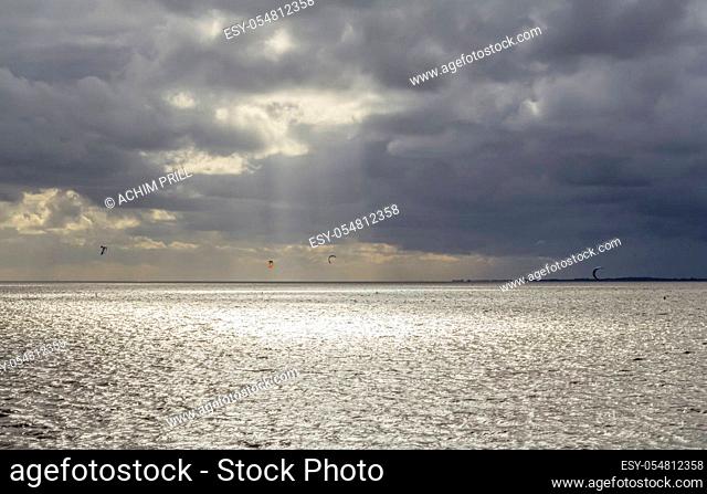 dramatic illuminated coastal scenery including some kitesurfers near Neuharlingersiel in Eastern Frisia, Germany