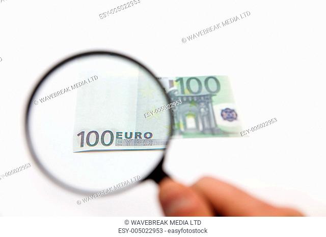 Hand holding magnifying glass over hundred euro note