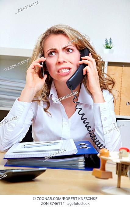 Wütende Geschäftsfrau im Büro telefoniert mit zwei Telefon gleichzeitig