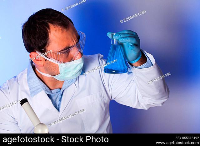 Scientist is doing research at the work, man holds the test tube with liquid