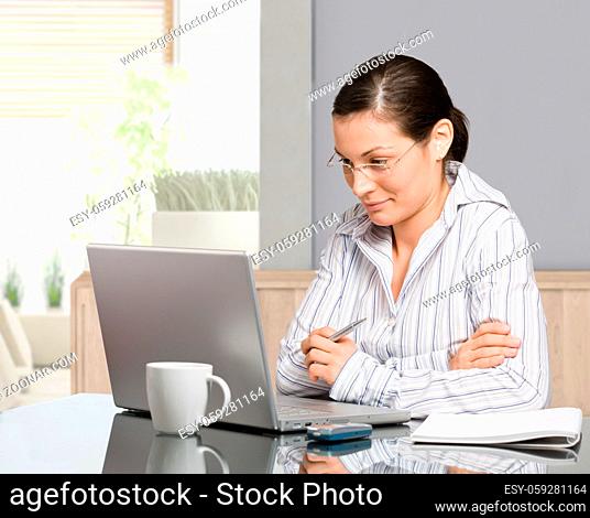 Young woman sitting at desk working with laptop computer at home, smiling
