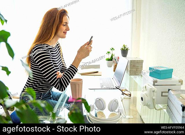 Young woman using smartphone at desk at home