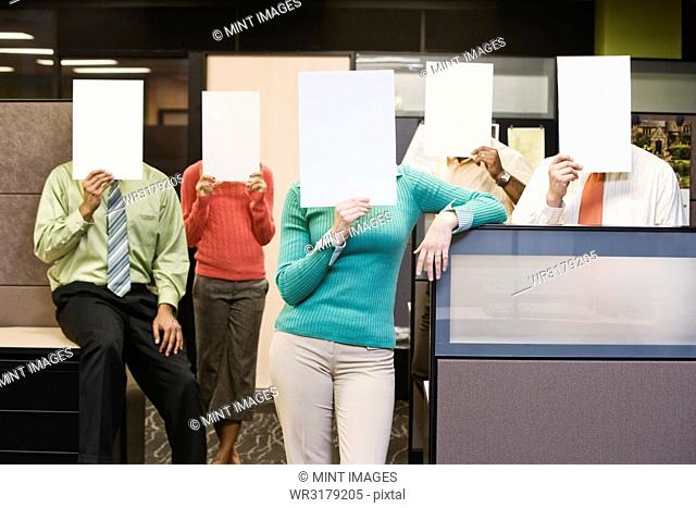 Team of business people standing with blank pieces of paper in front of their faces