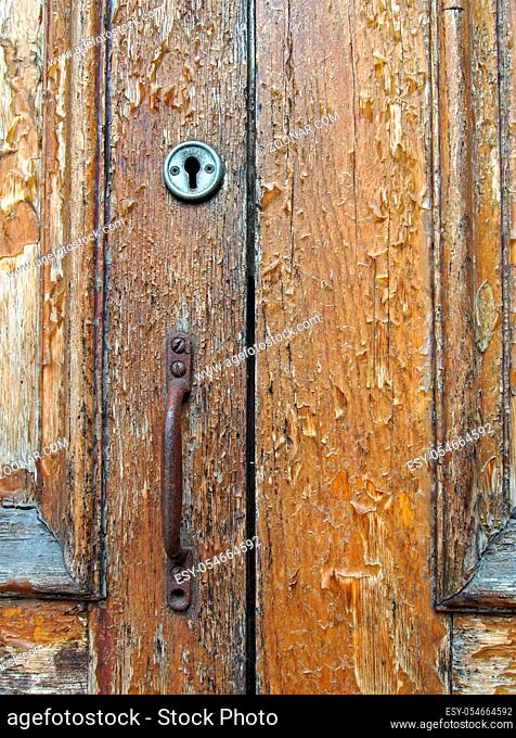 close up of an old brown varnished peeling wooden door with keyhole and rusty handle