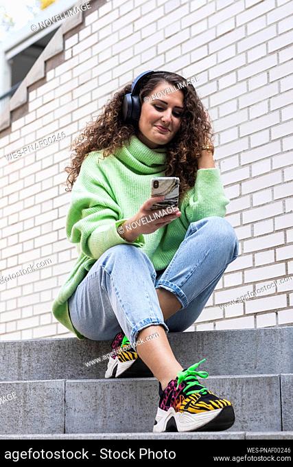 Young woman enjoying music while using mobile phone on steps