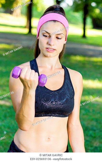 Fitness Slim Woman Training with dumbbells. Female practicing using hand weights outdoor. Healthy lifestyle workout concept on beautiful summer day