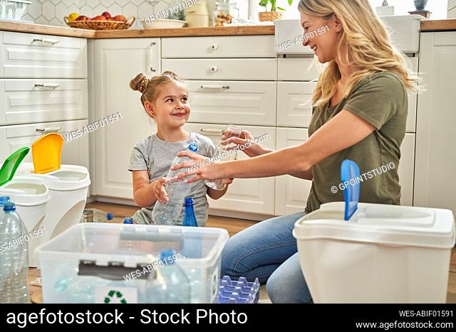 Smiling mother and daughter separating garbage together at home